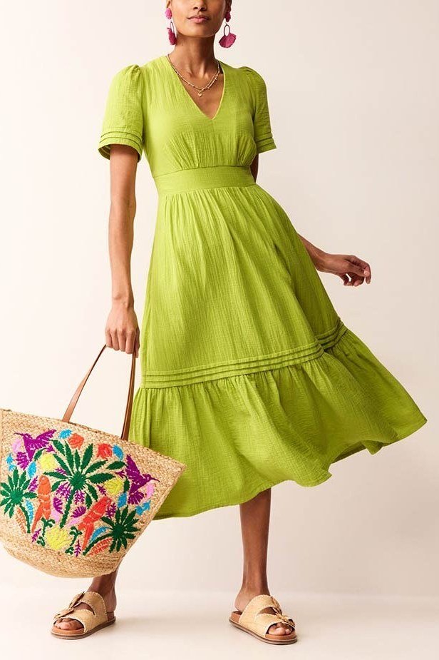 Woman in a lime-green short-sleeve midi dress with a colorful embroidered straw tote, studio shot - summer dress for women over 50