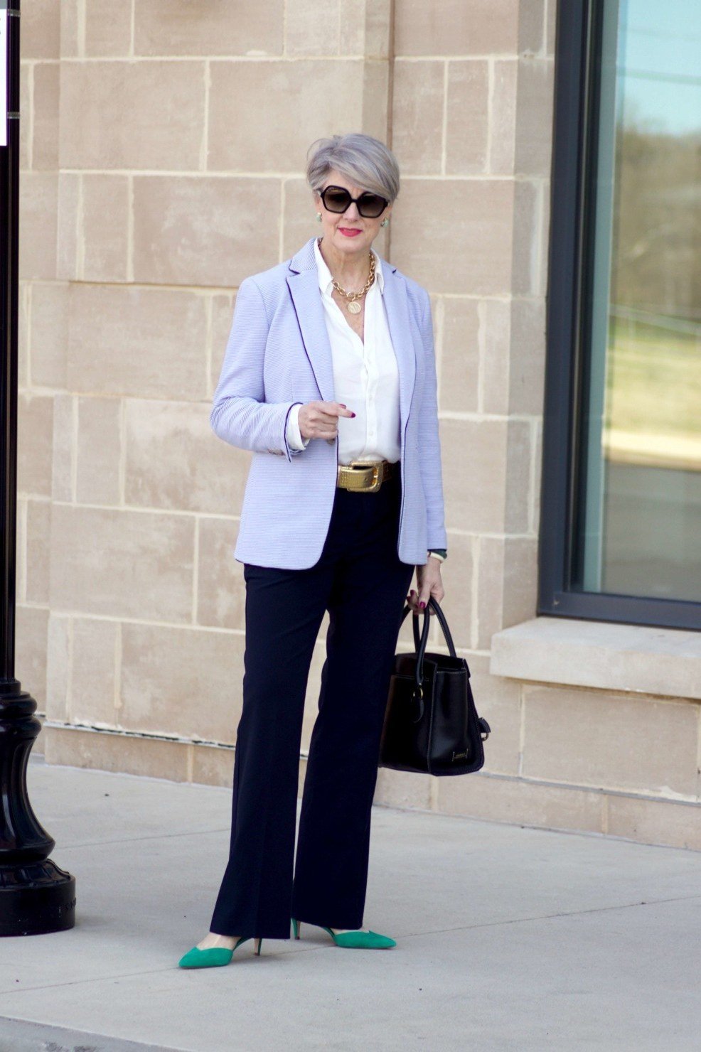 Woman over 60 in a light blue blazer with navy trousers and green flats