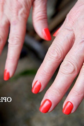 Warm coral red nail polish shade on older hands