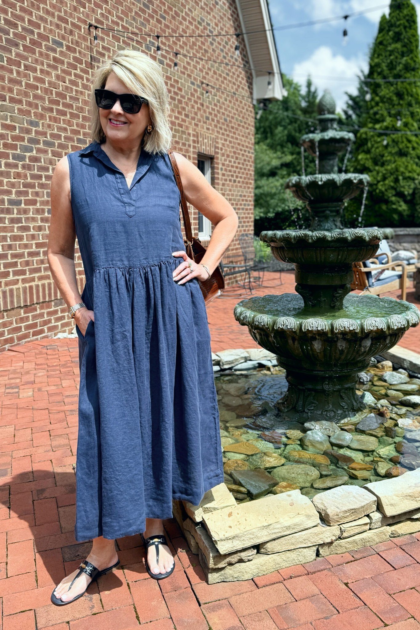 Woman in a blue chambray sleeveless shirt dress, standing by an outdoor fountain - summer dress for women over 50