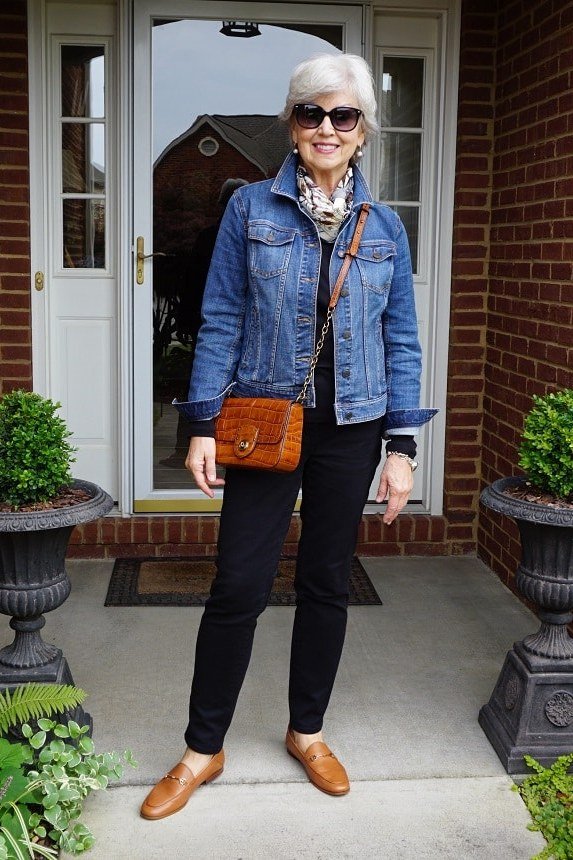 Woman over 50 wearing denim jacket with black pants and orange bag, everyday casual outfit idea