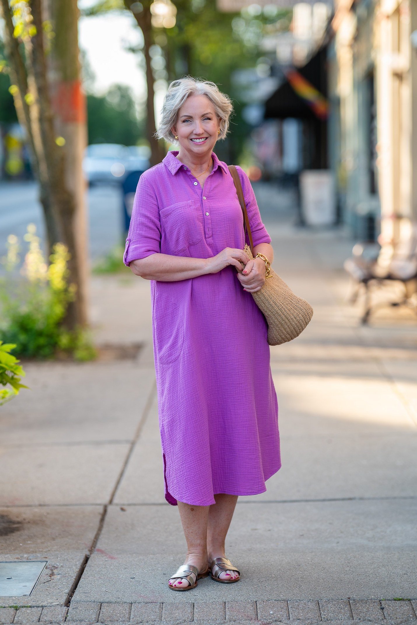 Woman in a purple short-sleeve shirt dress with a straw tote, city street - summer dress for women over 50