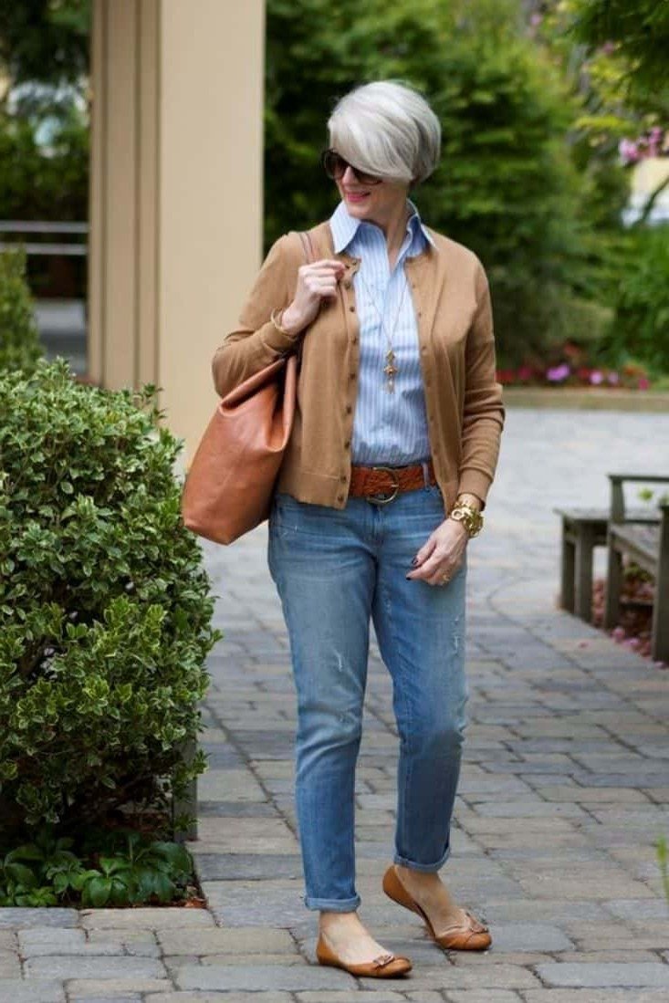 Woman over 60 wearing camel jacket, light blue shirt, medium jeans, tan bag