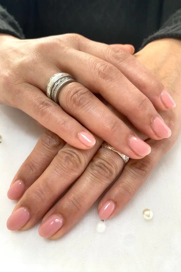 Blush pink glossy nails on mature hands with rings for women over 70