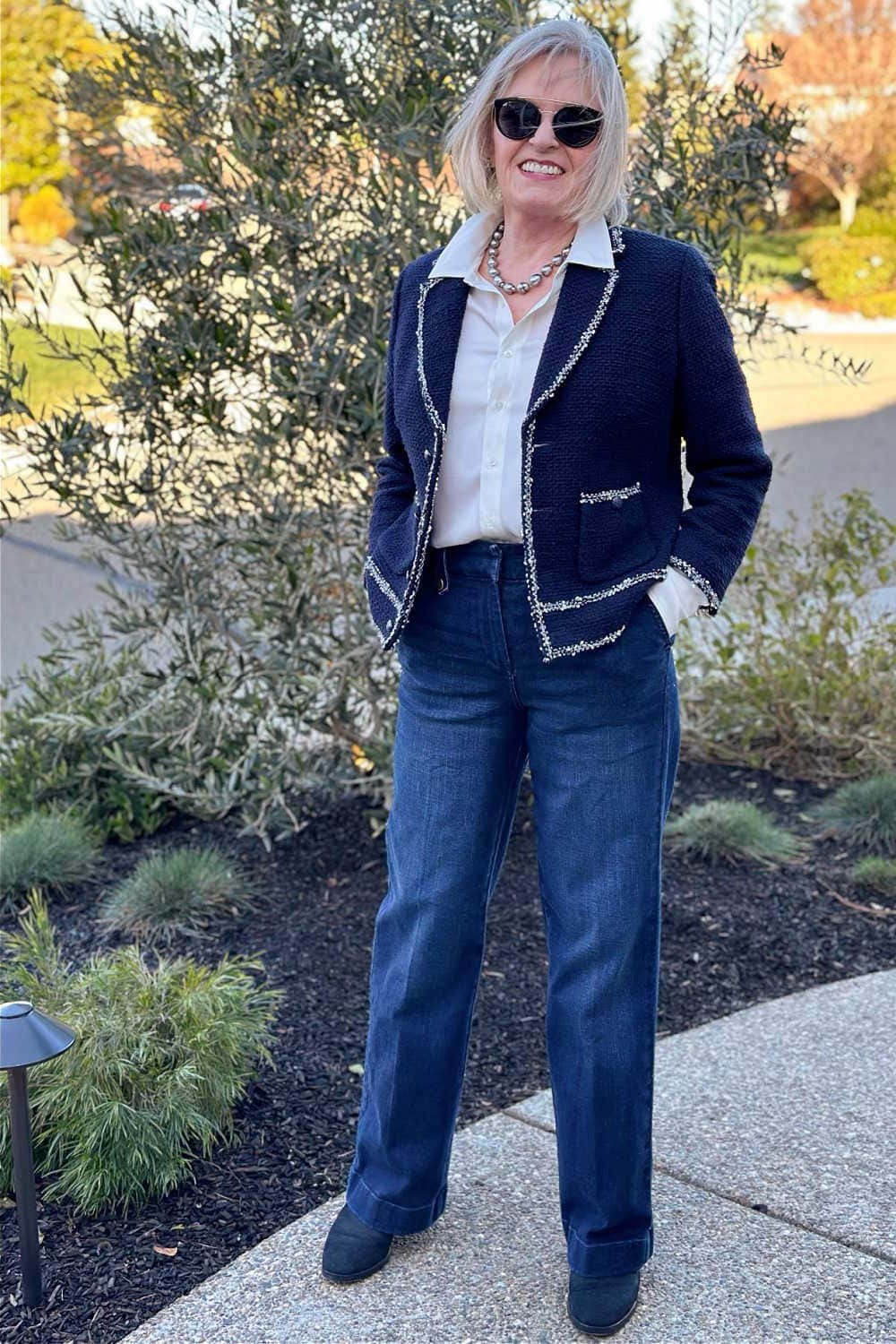 Woman over 50 wearing Navy tweed jacket with white shirt and jeans outdoors.