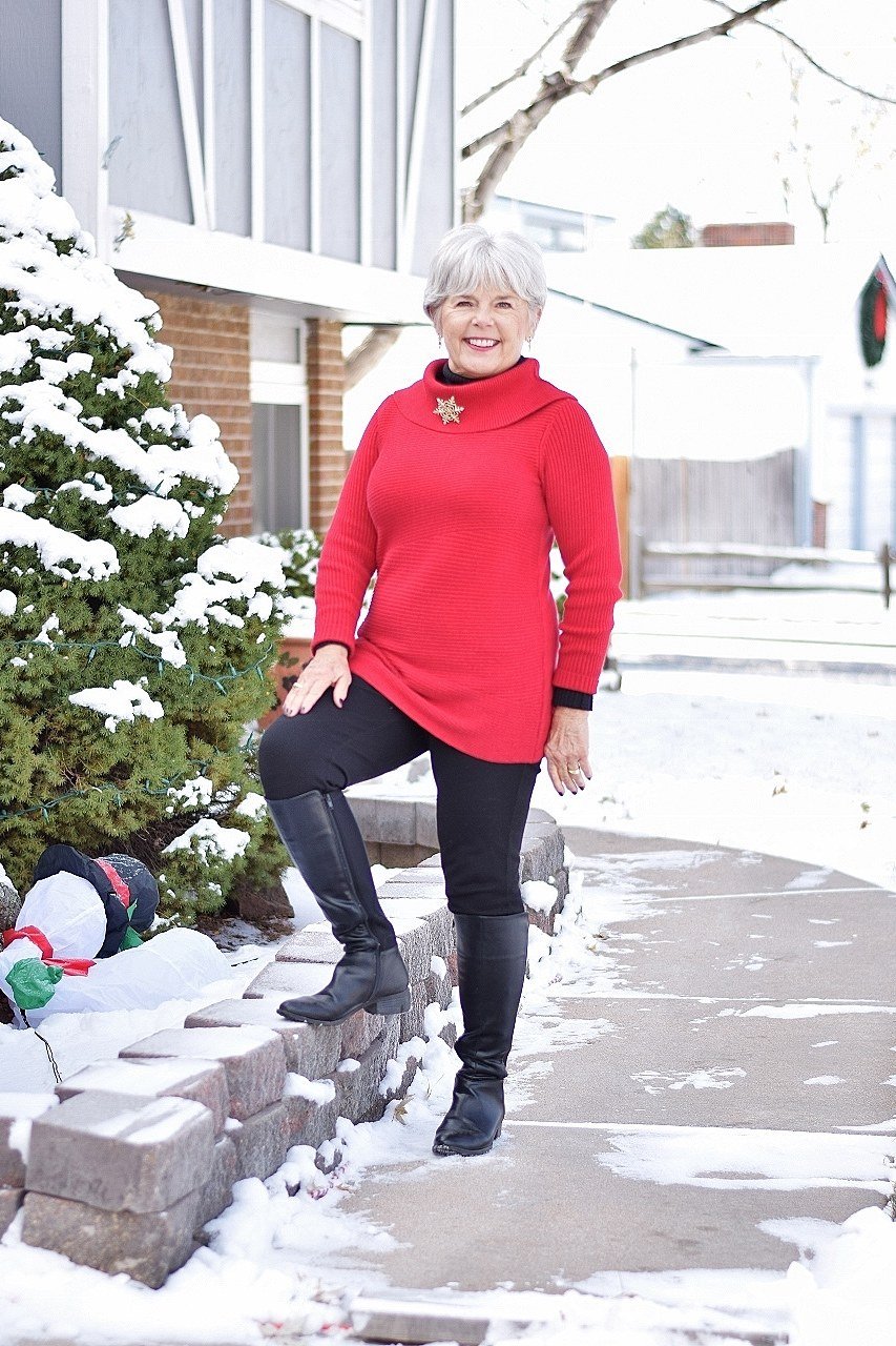 Stylish winter outfit for women over 60: red turtleneck sweater with black leggings and boots in snow