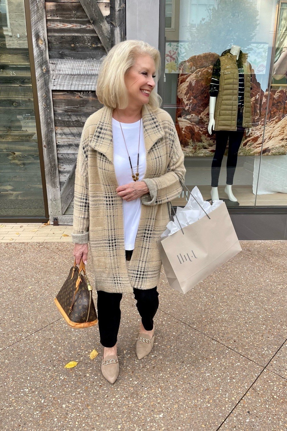 Brown plaid wool coat with white top and black leggings, shopping bags in hand