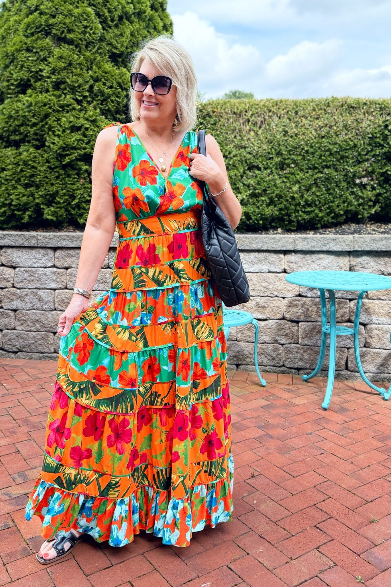 Blonde woman in a vibrant red-and-orange floral sleeveless maxi dress, brick patio - summer dress for women over 50