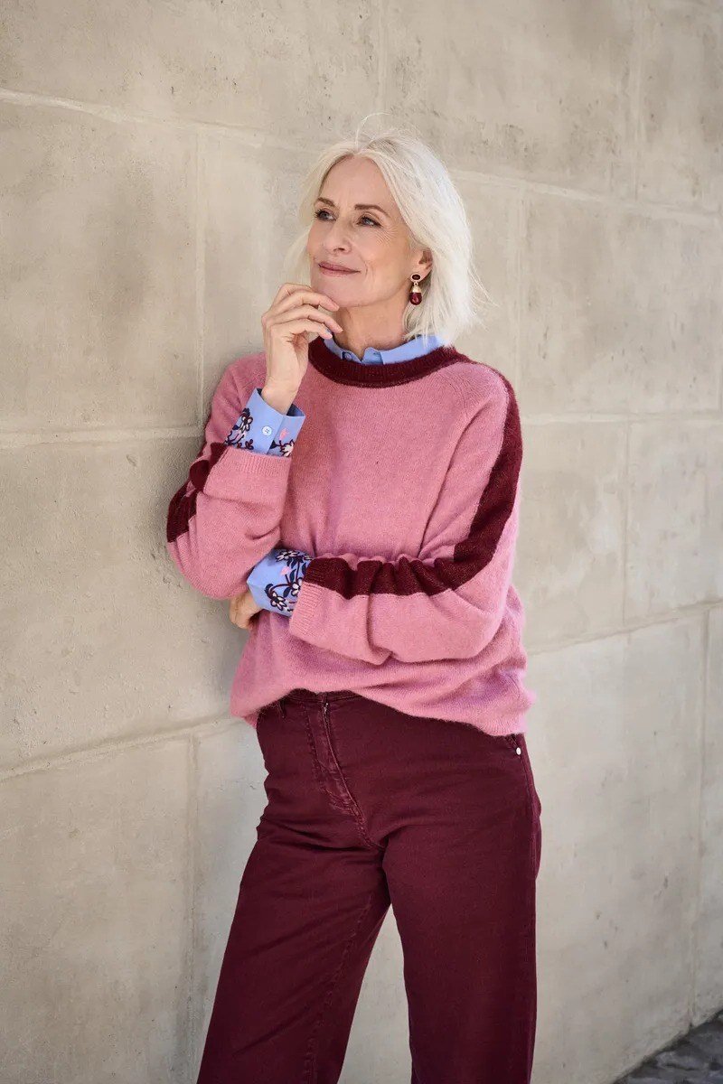 Woman over 60 in a pink and burgundy color-block sweater with burgundy trousers
