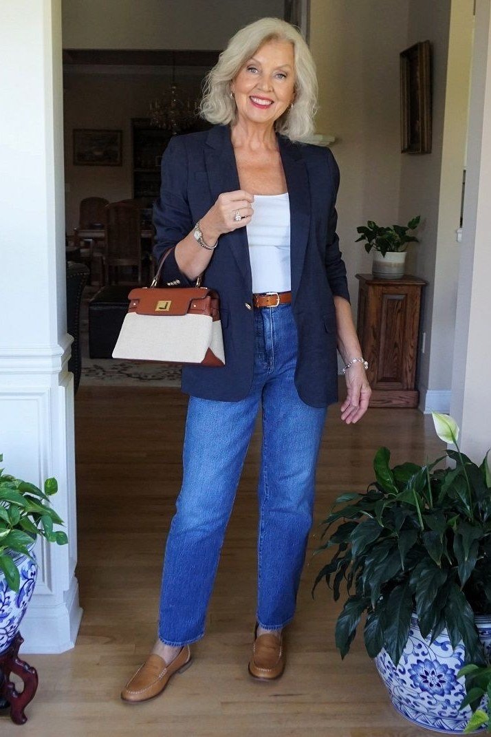 Woman over 60 wearing navy blazer, white tee, medium jeans, brown loafers, doorway