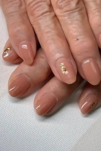Taupe nails with gold glitter accent nail on mature hands for women over 70