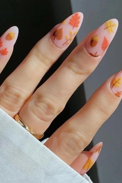 Long almond nails in soft peach with tiny autumn leaf decals, glossy fall elegance.