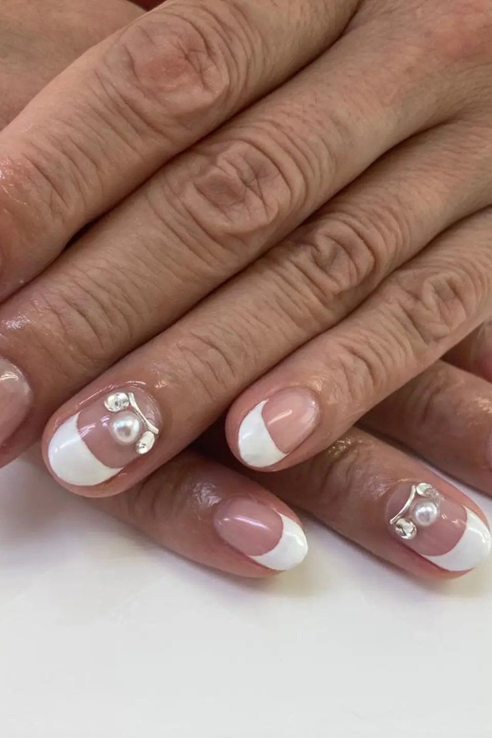 French manicure with white floral and pearl nail art on mature hands