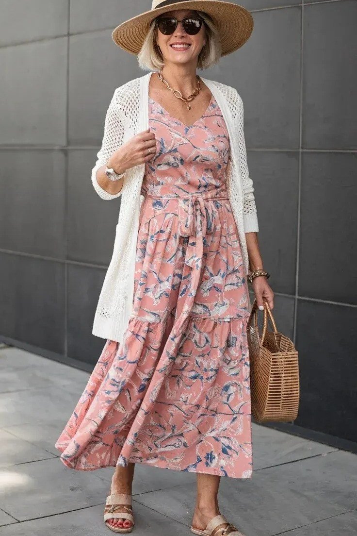 Woman in a pink floral maxi dress with a white cardigan and sun hat, studio shot - summer dress for women over 50