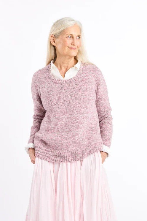 Older woman wearing a pink fuzzy sweater with a pink pleated midi skirt