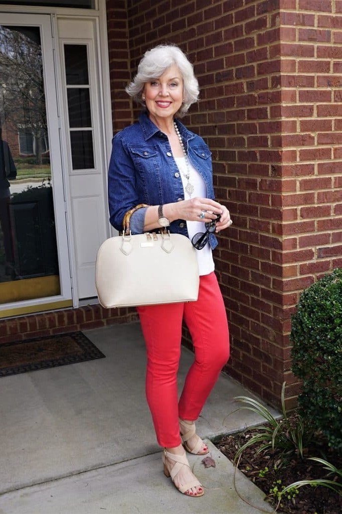 Woman over 50 wearing denim jacket with red pants and cream tote, everyday casual outfit idea