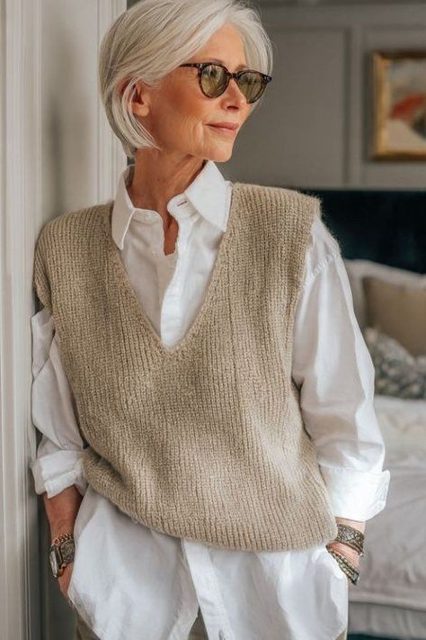 Oatmeal knit vest over white shirt standing indoors, cozy sweater outfit idea for women over 70