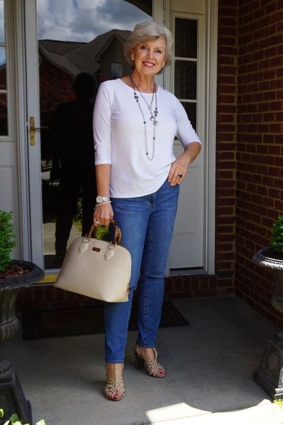 Woman over 60 wearing white top, medium jeans, cream tote