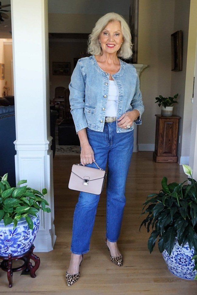 Woman over 50 wearing light denim jacket with blue jeans and white clutch, everyday casual outfit idea