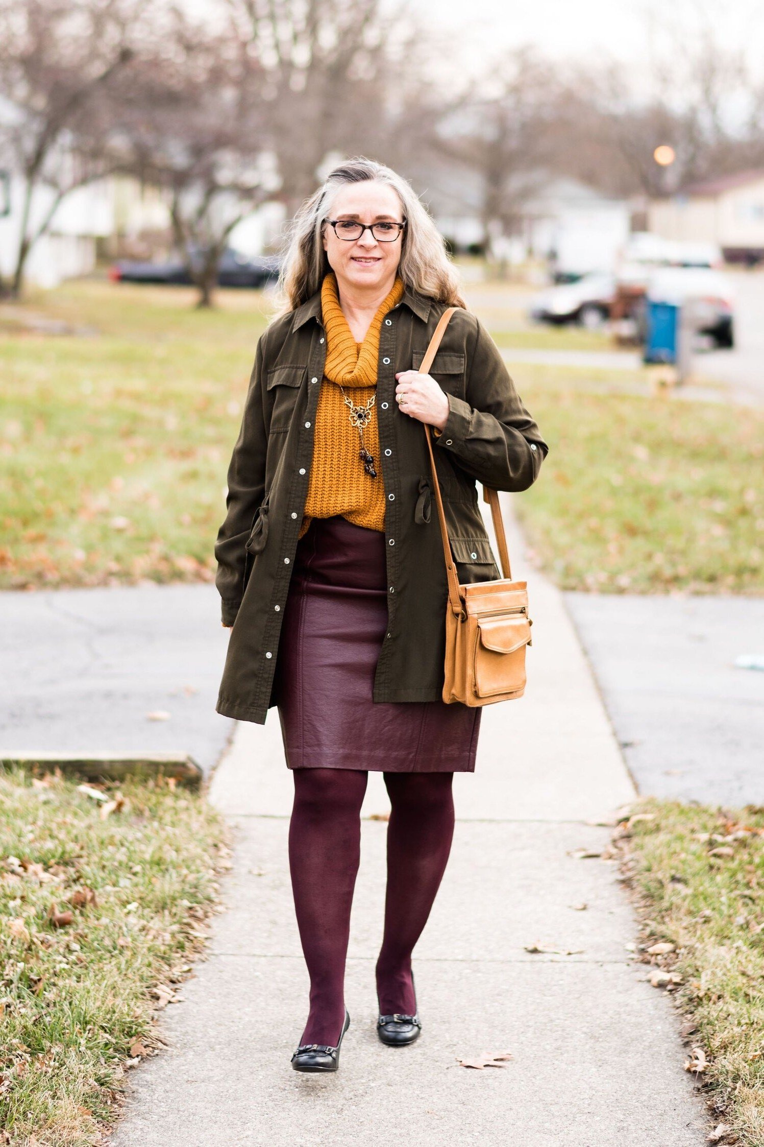 older woman in olive jacket with mustard top, burgundy leather skirt and burgundy tights