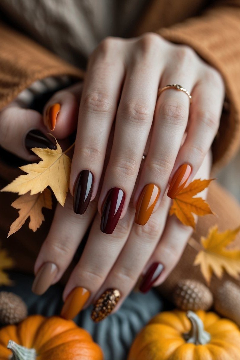 Plum and burnt orange short nails photographed among golden autumn leaves and mini pumpkins.