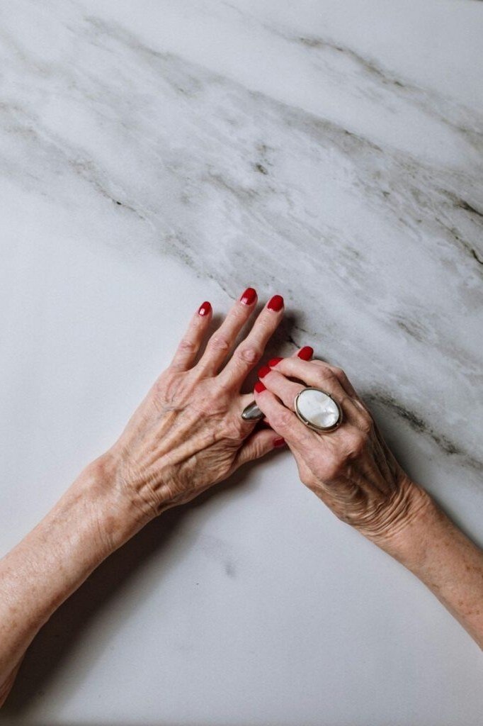 glossy red nails resting on marble for older women