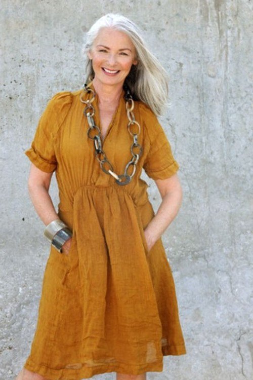 Older woman with long white hair in a mustard-yellow short-sleeve linen midi dress, studio shot - summer dress for women over 50