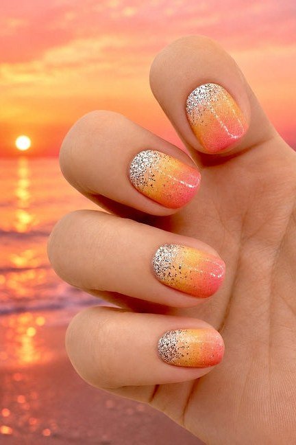 Sunset Glitter Ombre on Almond Nails - Peach and coral ombre covers these medium almond nails, dusted with fine gold glitter near the tips.