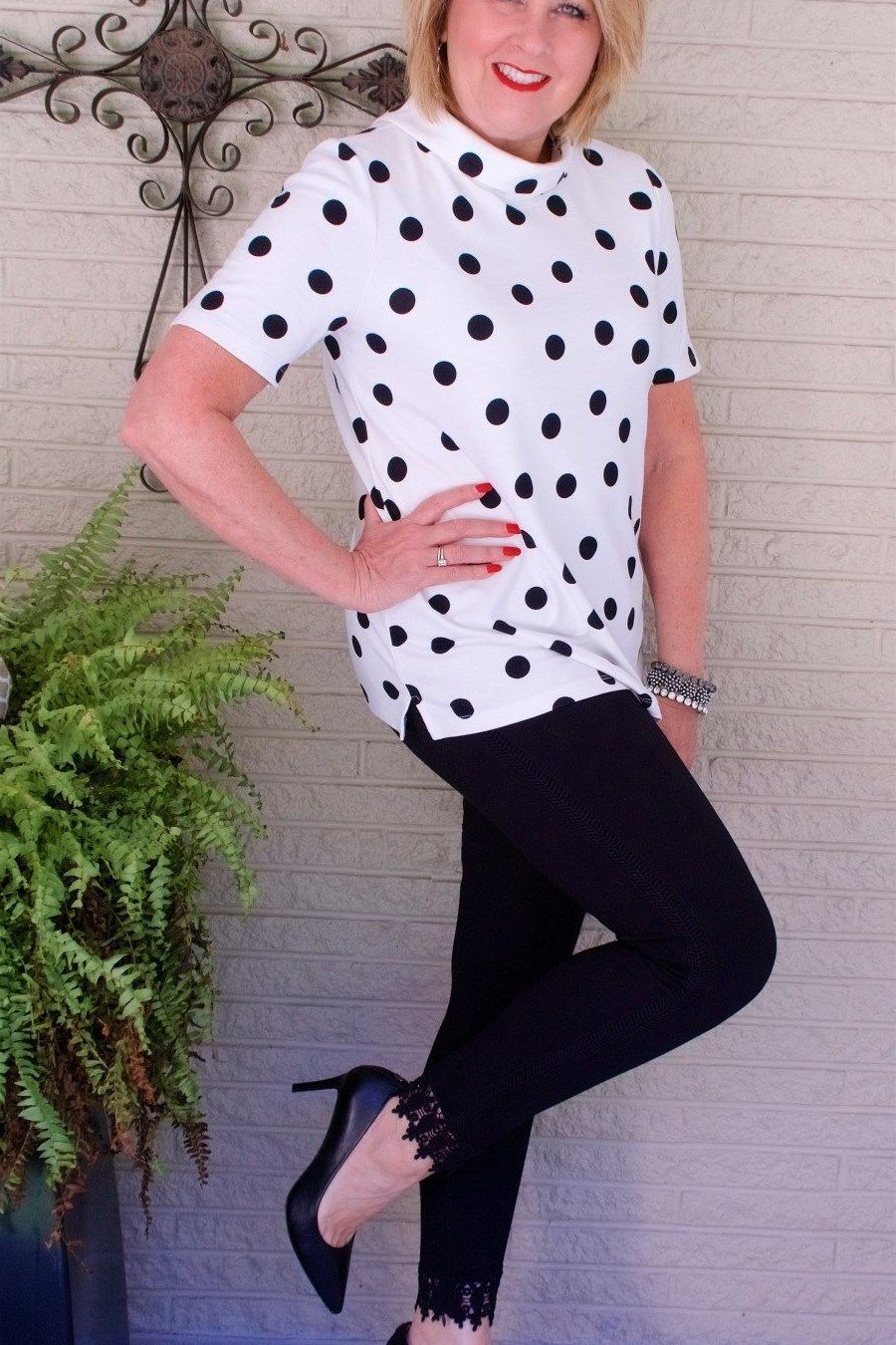 White polka-dot blouse, black trousers, playful pose interior, chic night out outfit for women over 50