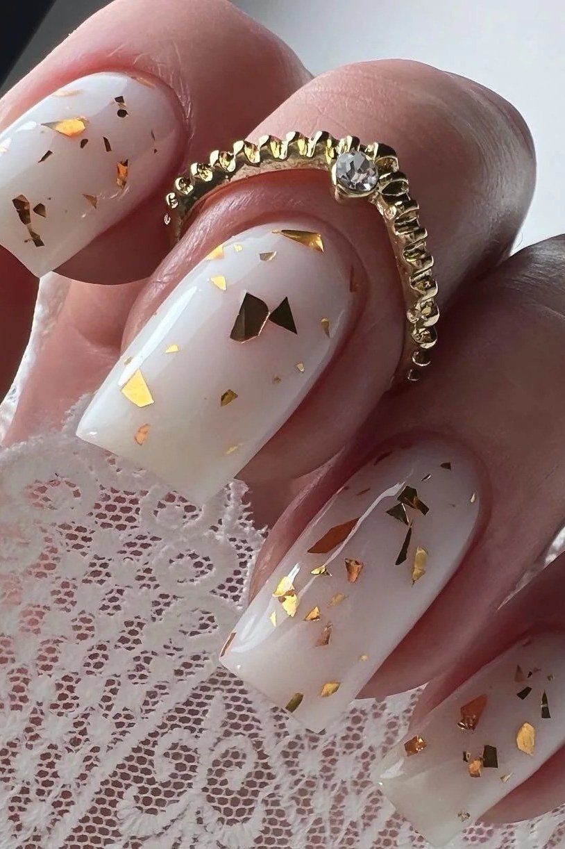 Milky white nails with gold flakes styled on lace