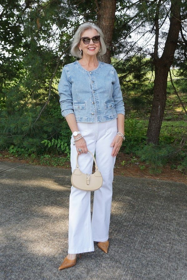 Woman over 50 wearing chambray shirt with white flare jeans and tan bag, everyday casual outfit idea