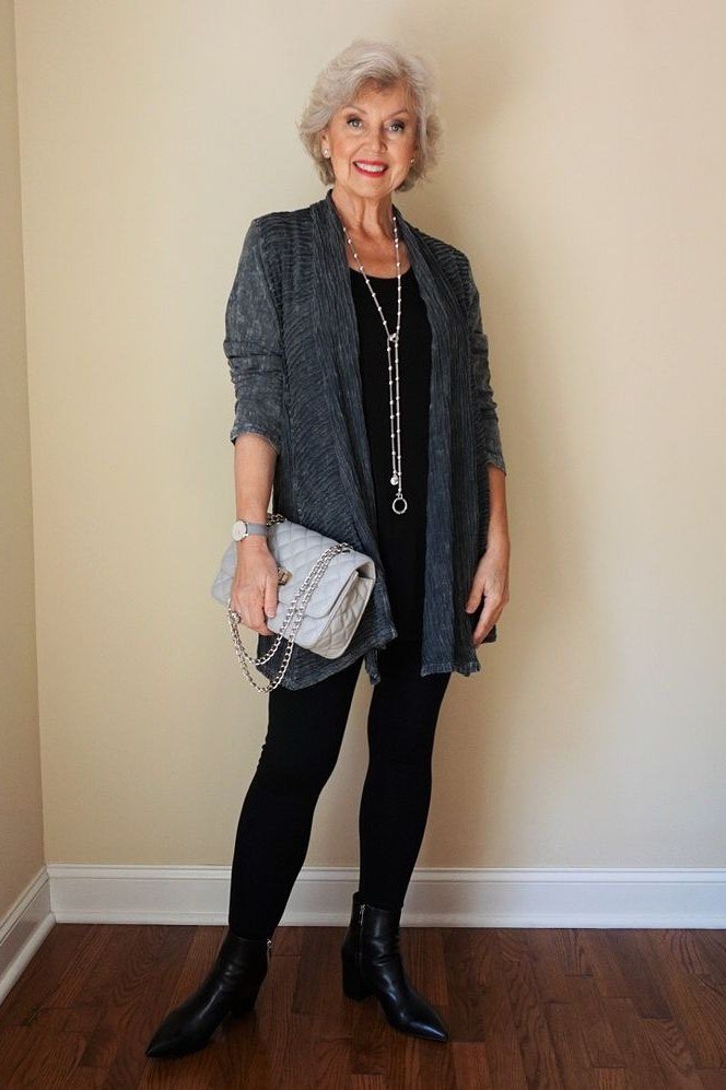 Woman over 50 wearing Grey blazer with black top, black pants and silver clutch indoors.