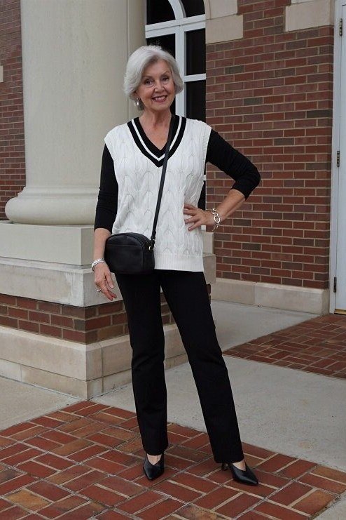 Black-and-white cricket-style knit vest over black turtleneck by brick wall, cozy sweater outfit idea for women over 70