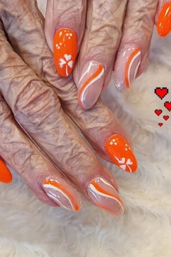 Bright orange almond nails with white daisy nail art on mature wrinkled hands.