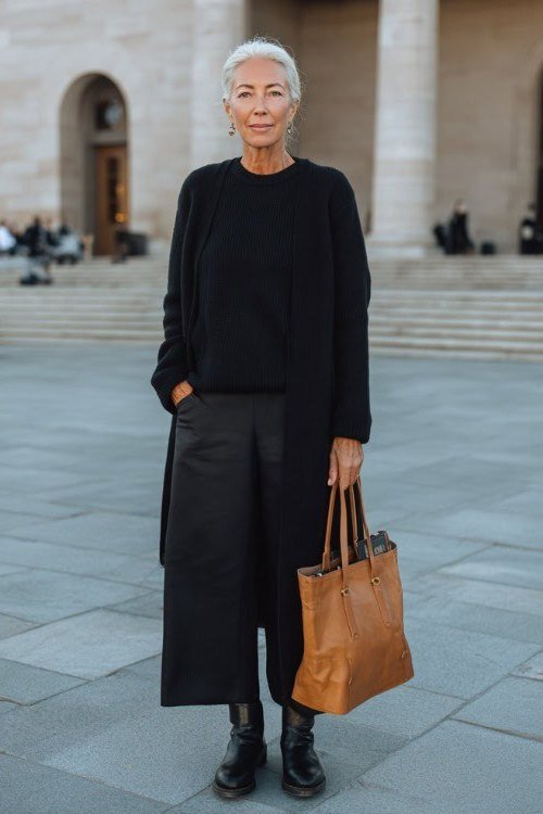 Woman over 60 in a black tunic with black culottes and a cognac bag
