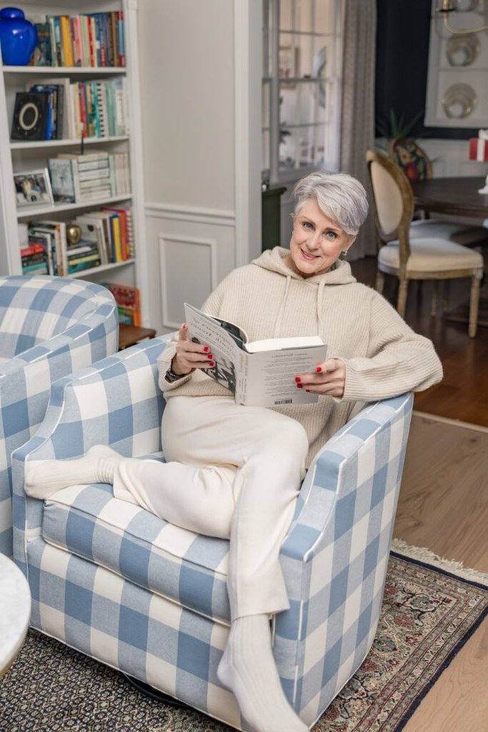 Stylish winter outfit for women over 60: cream cozy knit set reading in a blue armchair