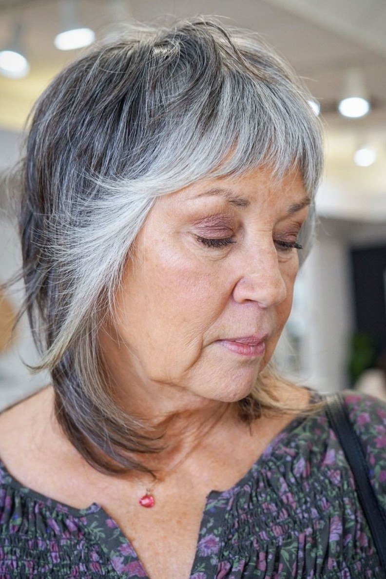 Gray shag haircut with bangs on an older woman, front view, medium hairstyle for women over 60