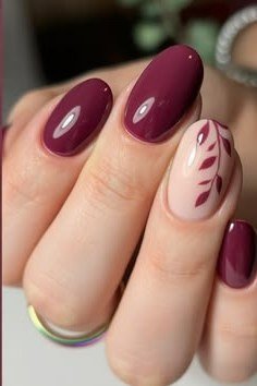 Deep plum almond nails with a single white leaf art accent nail, glossy fall design.