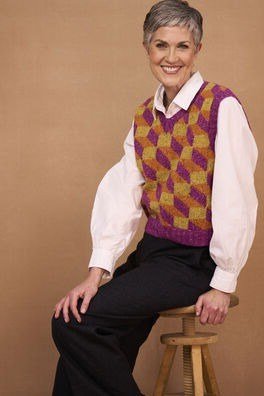 Purple-and-mustard argyle knit vest over pink shirt on stool, cozy sweater outfit idea for women over 70
