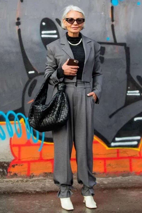 Older woman wearing a grey tailored suit with white sneakers on a city street