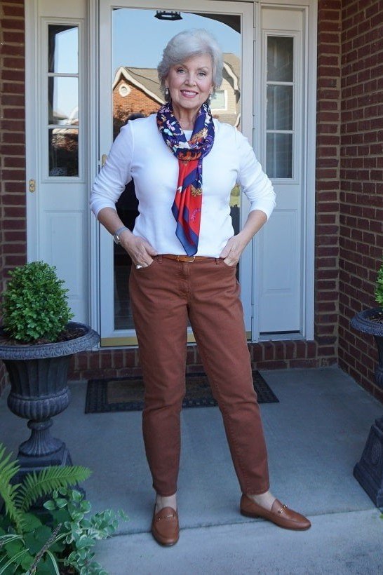 White shirt with rust wide trousers and colorful silk scarf, woman over 50