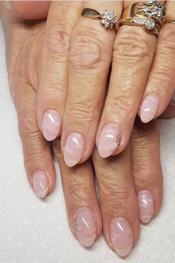 Sheer nude nails with gold rings on elderly hands