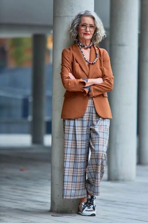 Woman over 60 in a rust blazer with plaid wide-leg trousers and sneakers