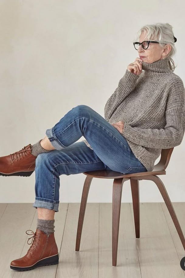 Stylish winter outfit for women over 60: gray turtleneck sweater with jeans seated on a chair