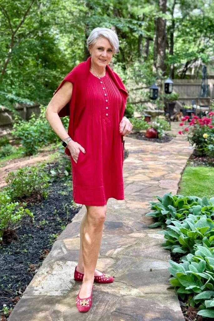 Woman over 50 wearing Red shirt dress with pink heels in a garden.