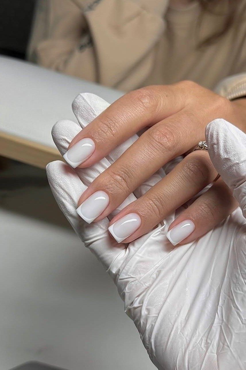 Fresh milky white manicure held by a gloved salon hand