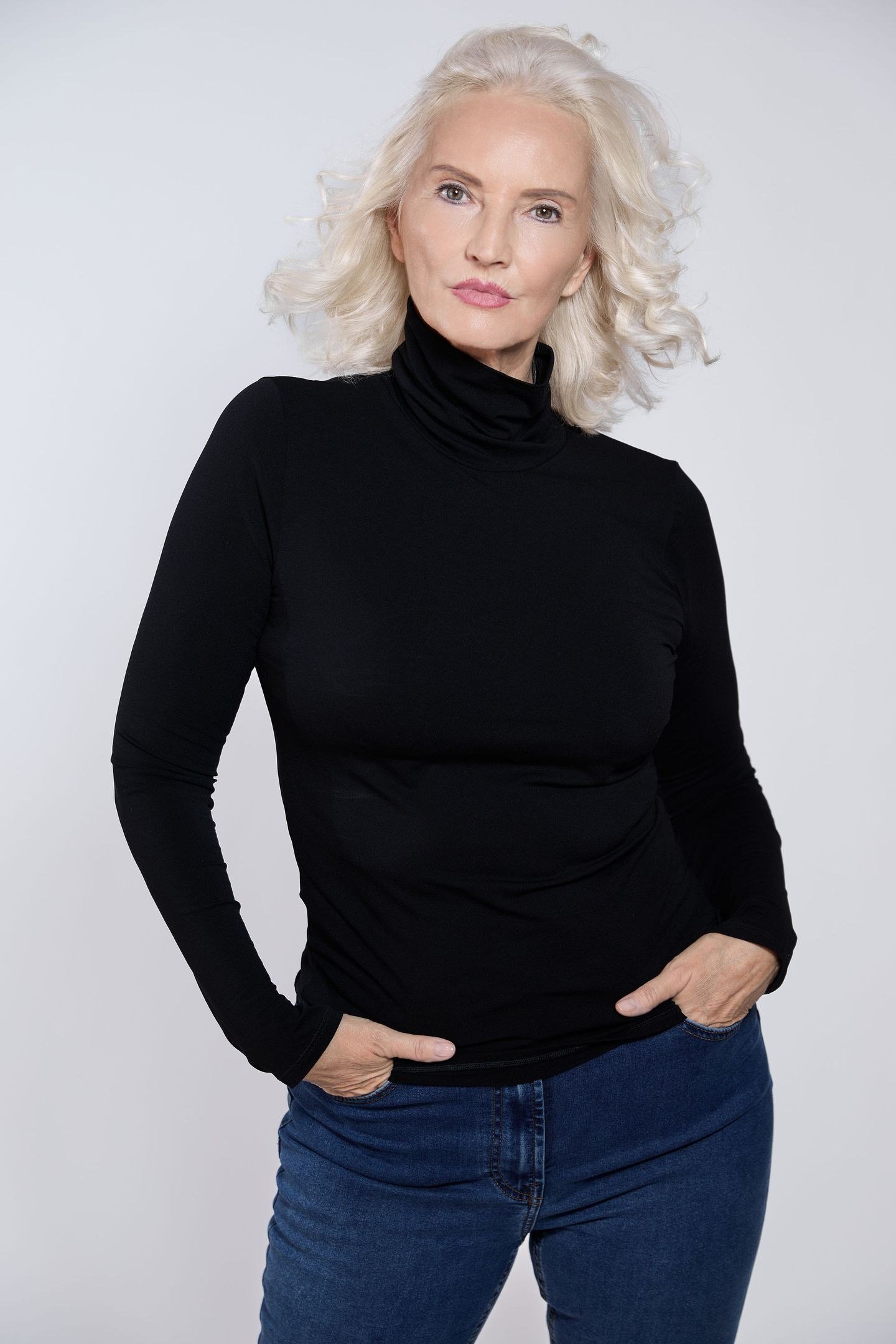 older woman in black turtleneck with blue jeans, studio portrait