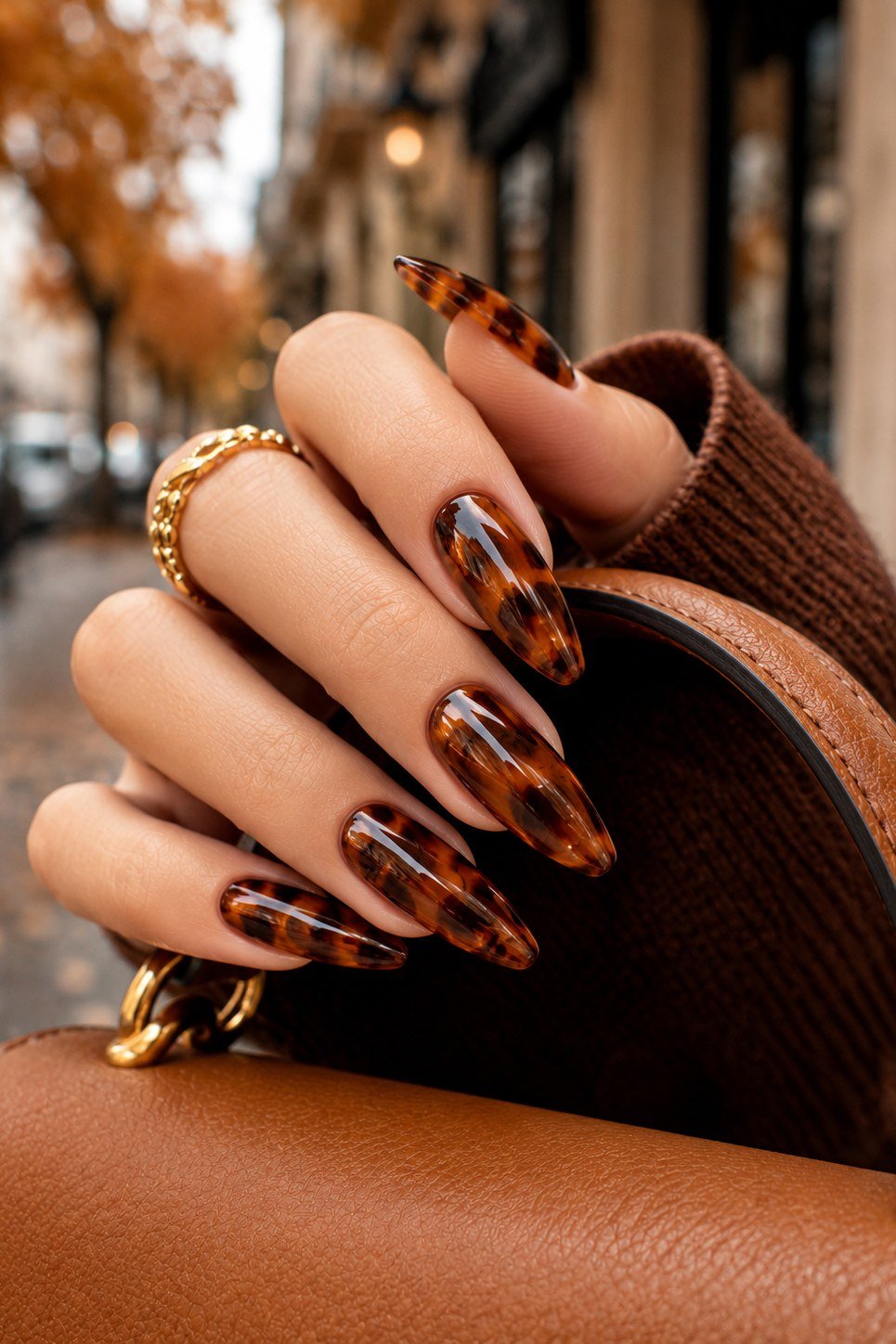 Tortoiseshell print, almond shape, long length, glossy, hand on tan leather bag, autumn street background, fall nail color for women over 40
