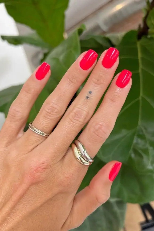 short oval, bright coral red, one hand with rings near green plant , for women over 60