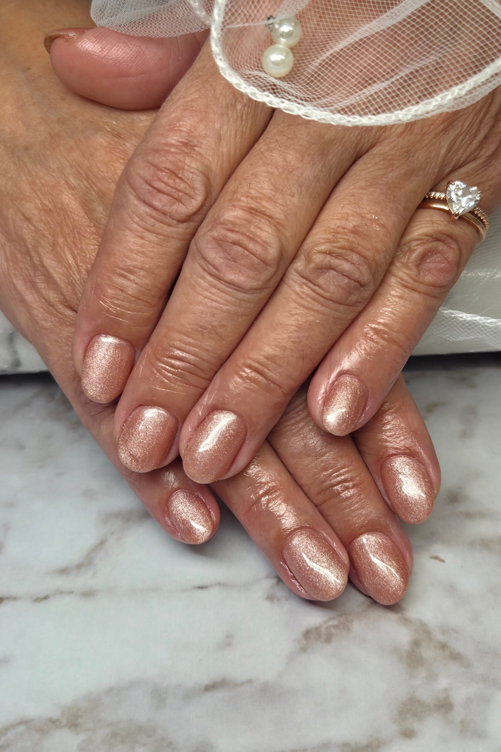 Rose gold metallic nails on mature woman's hands over marble